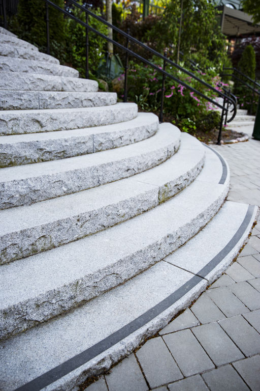 Trappa i grå råkilad granit i rundad form där ett steg längst ned har en svart kontrastrand.