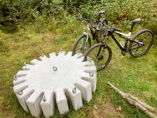 Cykelstället Kuggen på plats i ett skogsbryn med två mountainbikes parkerade.