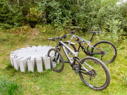Cykelstället Kuggen på plats i ett skogsbryn med två mountainbikes parkerade i cykelstället.