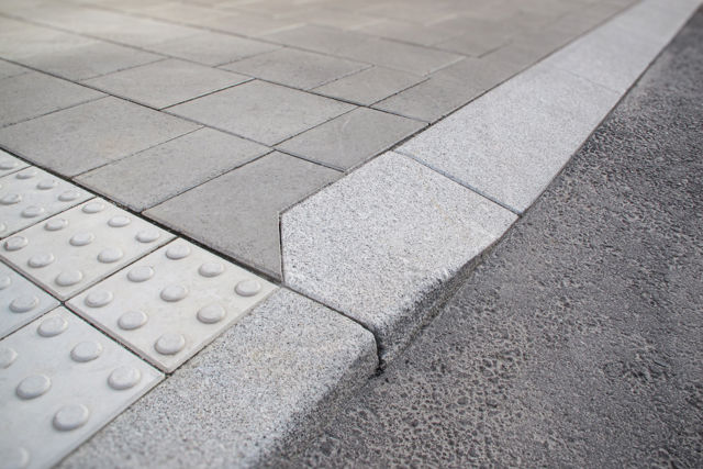 Portstens i natursten;kompletterad med taktila betongplattor med orienteringsmönster samt släta betongplattor i gångyta – i övergång mellan gångbana och körbana.