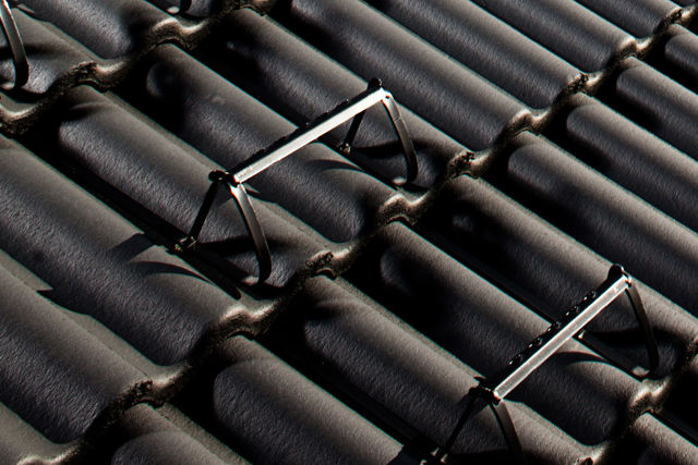 Ett utsnitt av ett villatak med svarta takpannor och bärläktsteg monterade.