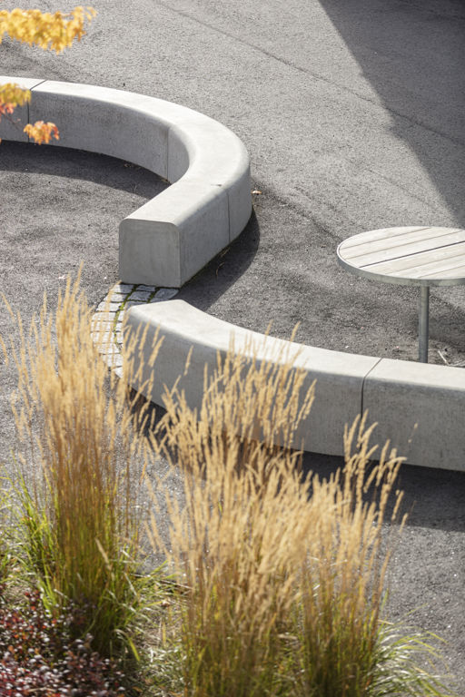 Flera Outline-bänkar bildar en ringlande orm på en skolgård med gul vass