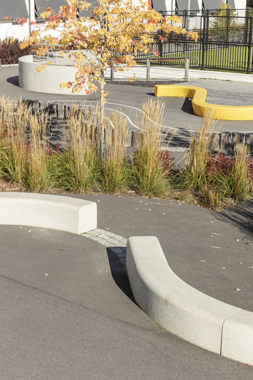 Flera Outline-bänkar bildar en ringlande orm på en skolgård med gula träd