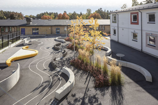 Flera Outline-bänkar bildar en ringlande orm på en skolgård med gula träd
