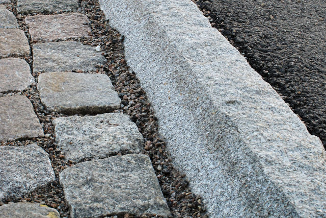 Granitkantsten RFF med råhuggen front och fasad överkant;monterad mellan asfalt och smågatsten.