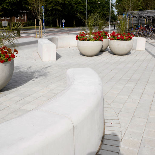 Flera Outline-bänkar som bildar ett mönster i form av slingrande mönster på ett torg med röda blommor i stora runda grå krukor