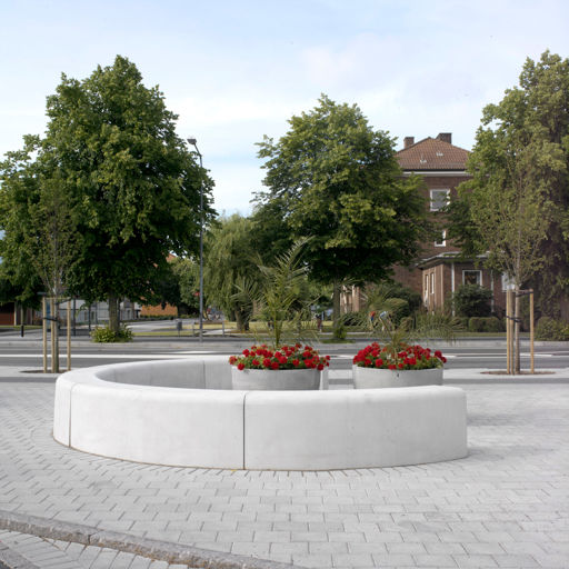 Flera Outline-bänkar som bildar ett mönster i form av en halvcirkel på ett torg med röda blommor i stora runda grå krukor i mitten