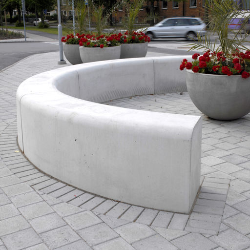 Flera Outline-bänkar som bildar en halvcirkel på ett torg med röda blommor i en kruka i mitten och i bakgrunden