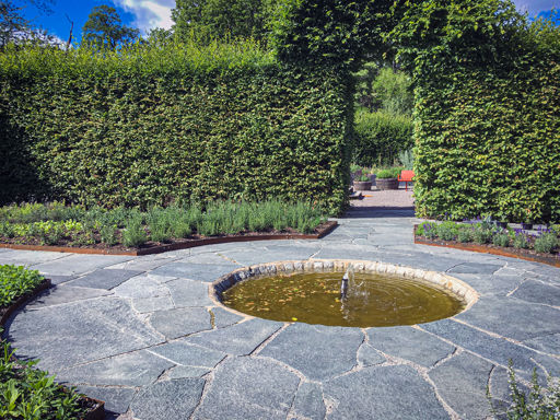 Offerdal oregelbundet skiffer på plats i parmiljö med en grön tujahäck bakom och en fontän i mitten