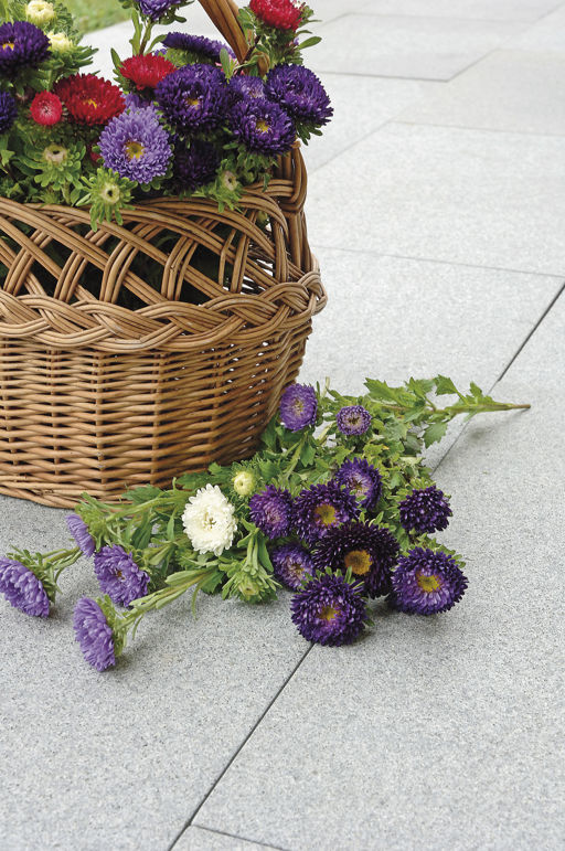 En korg med blommor står på en en yta med ljusgråa granithällar.