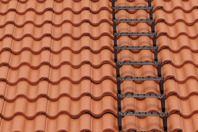 Ett utsnitt av ett villatak med tegelröda takpannor och bärläktsteg monterade.